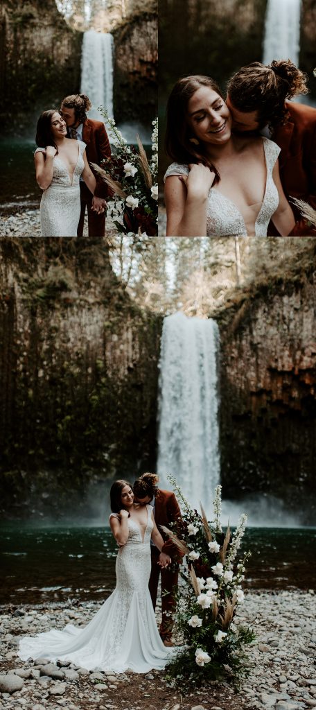 Groom wearing a burnt orange wedding suit kissing his bride on the neck in front of their Oregon waterfall elopement location.