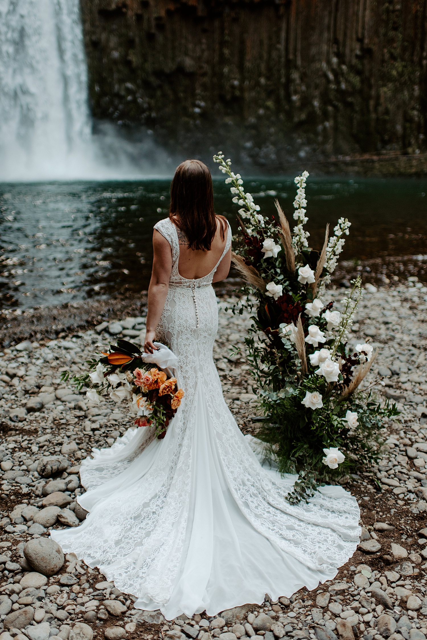 Bride facing away from the camera with a backless wedding dress, long lacey train, and boho florals.
