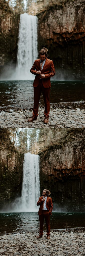 Groom wearing a burnt orange wedding suit in front of a waterfall in Oregon.