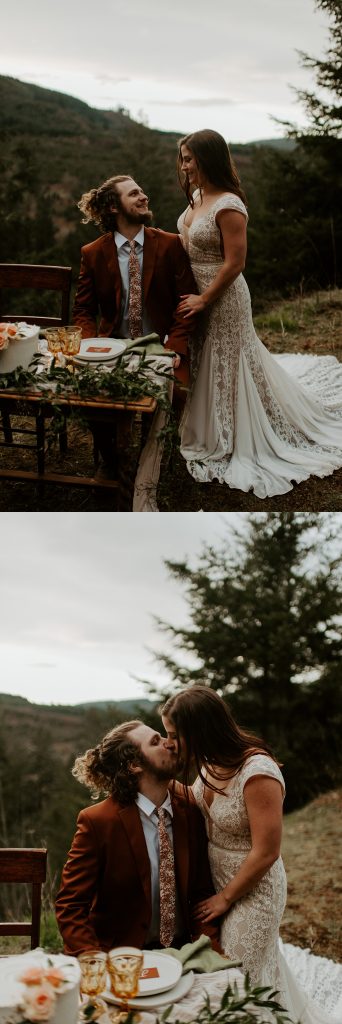 Married couple kissing by their small elopement tablescape with a view of a valley behind them.