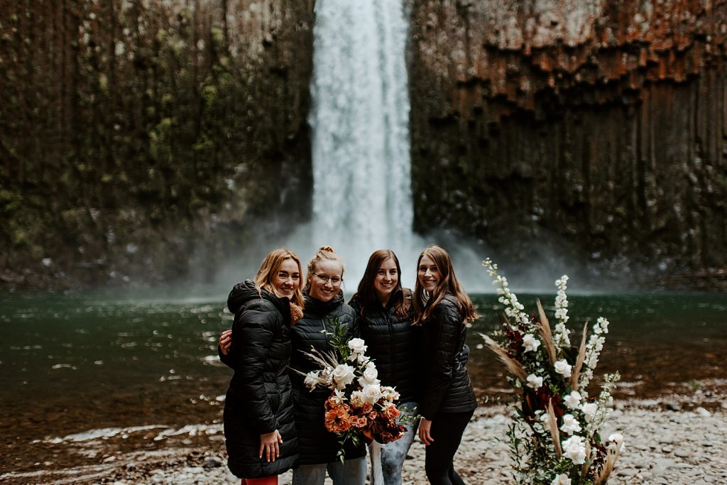 Oregon Elopement Vendor Team posing in front of a waterfall, which was the elopement location for a bride and groom.