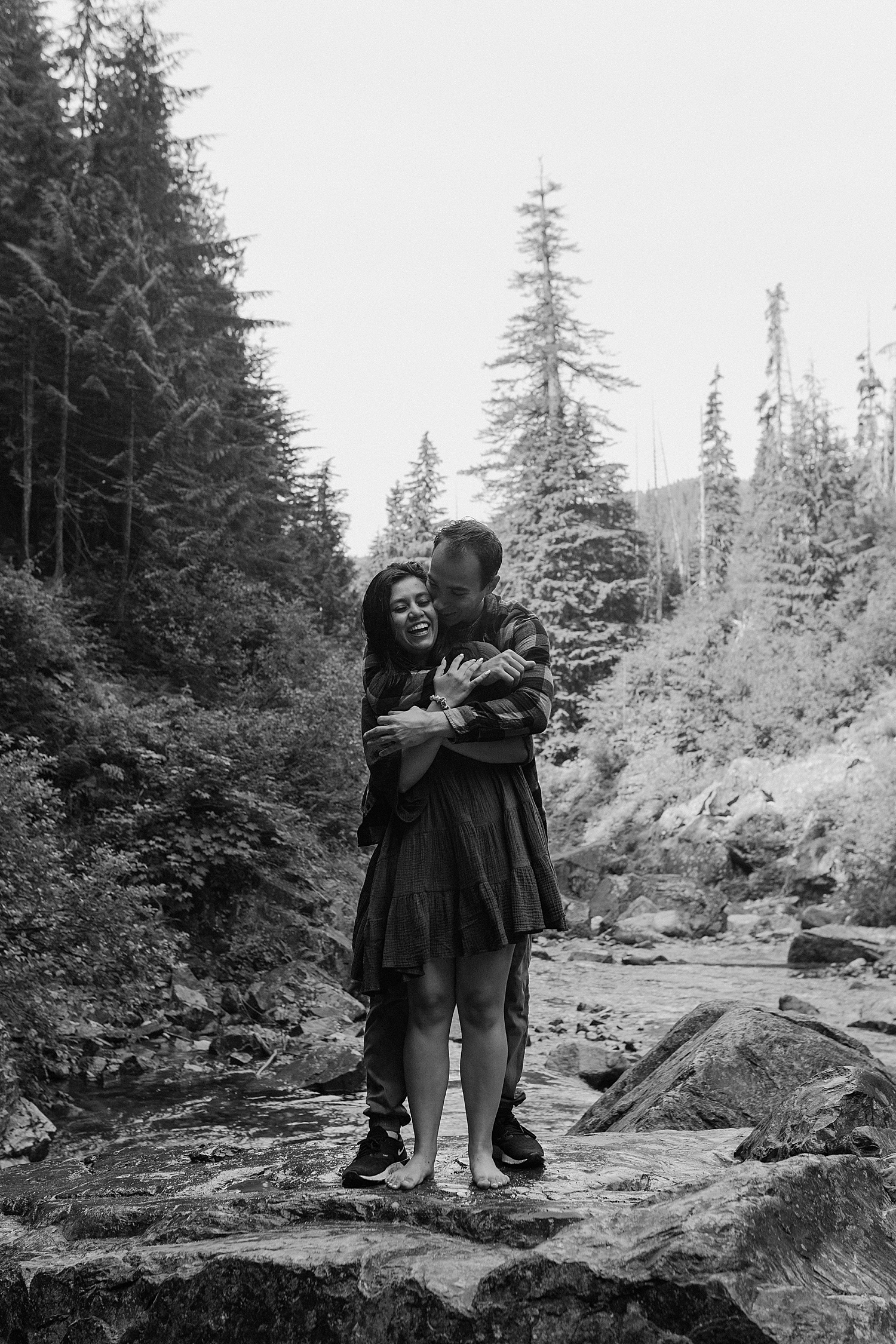 Black and white photo of a couple hugging while standing on a rock
