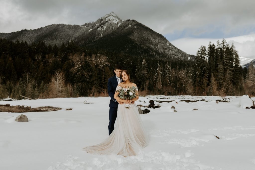Eloping couple embracing in the snow with a mountain backdrop