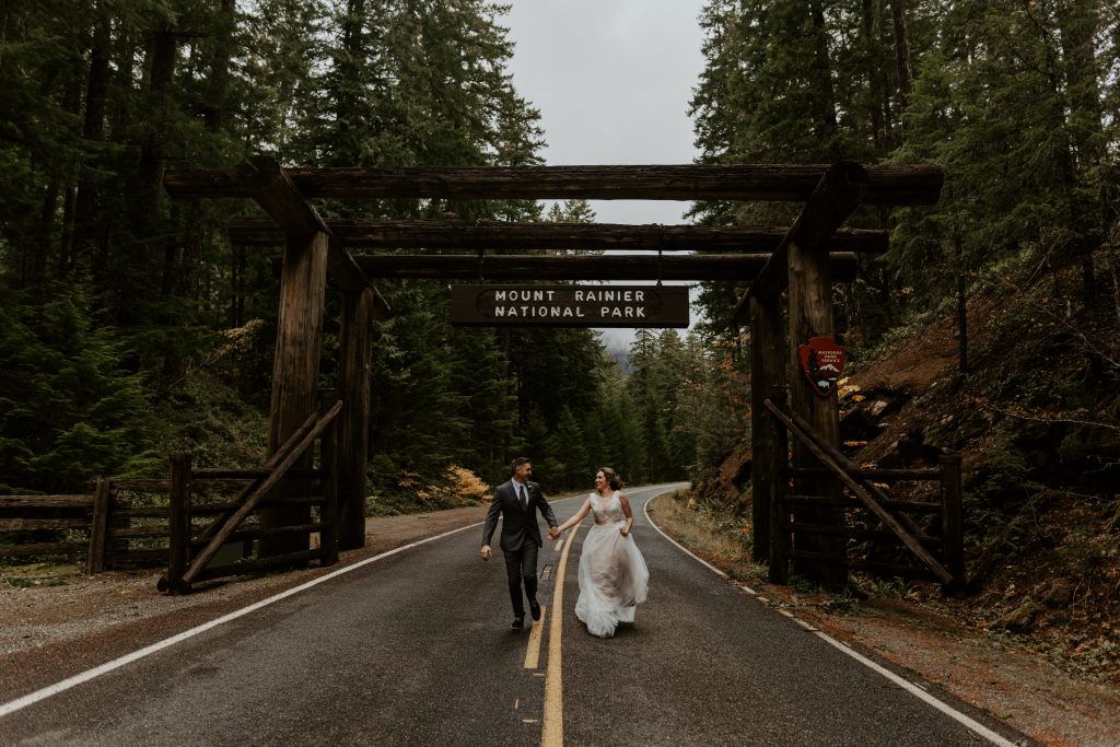 Married couple running under the Mount Rainier National Park sign