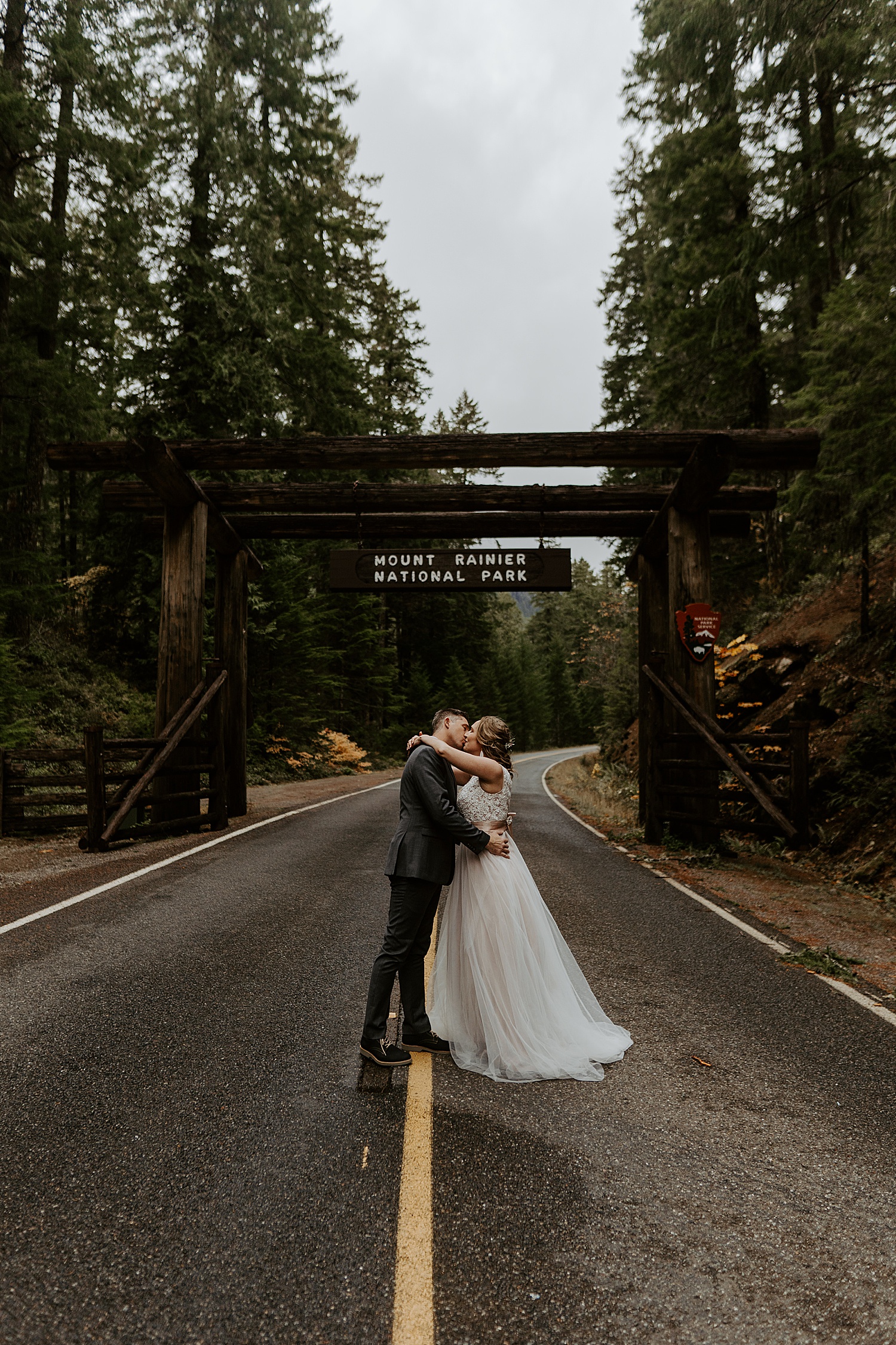 Newly married couple kissing in front of the Mount Rainier National Park sign
