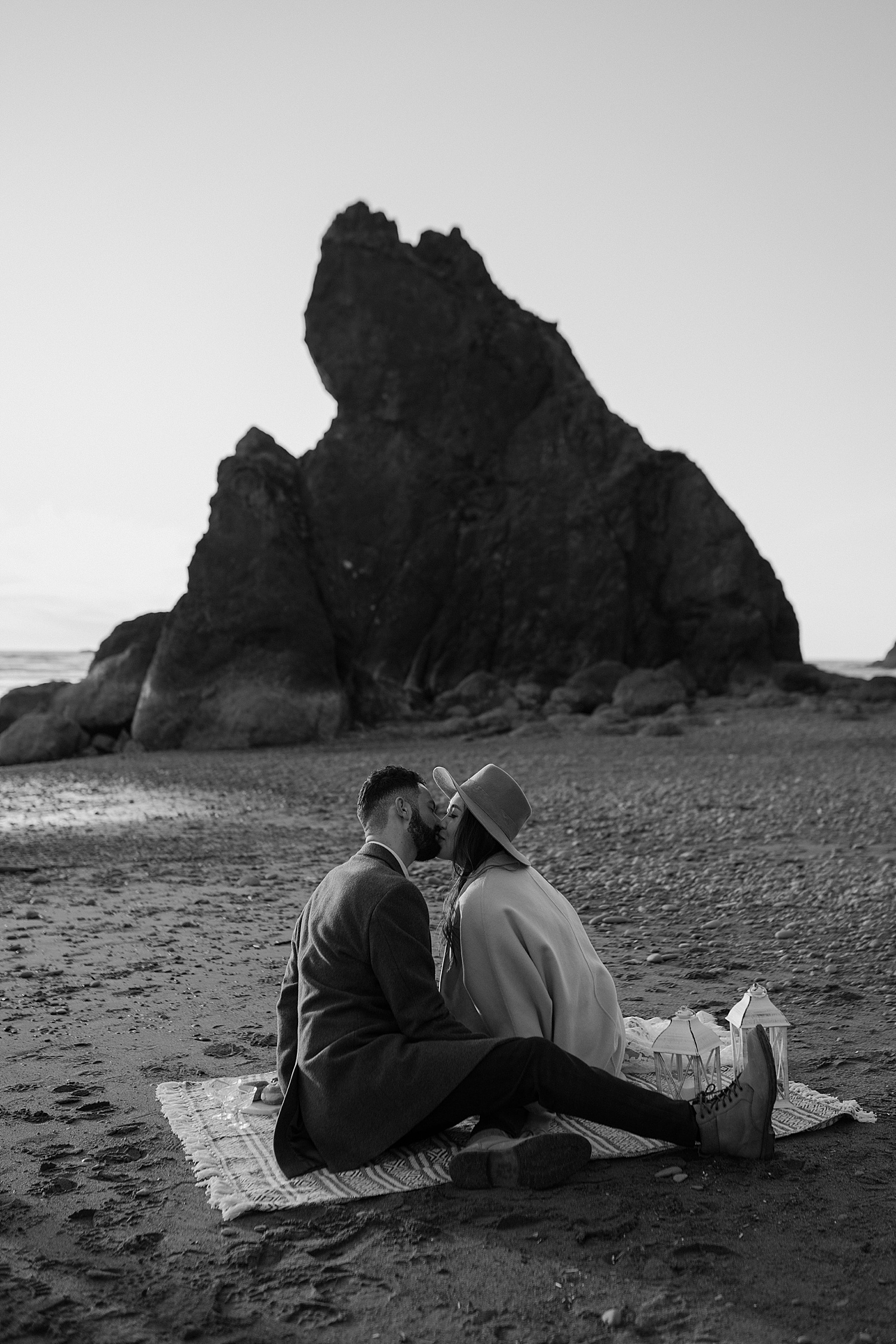 black and white image of a couple kissing while sitting on the beach