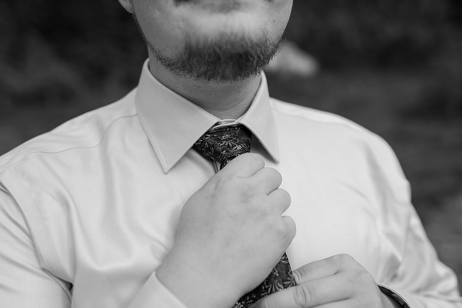 black and white photo of groom putting his tie on