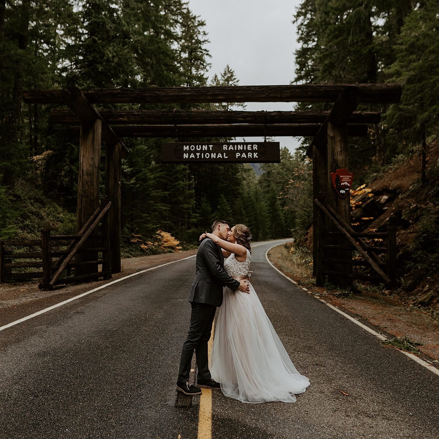 Newly married couple kissing in front of the Mount Rainier National Park sign
