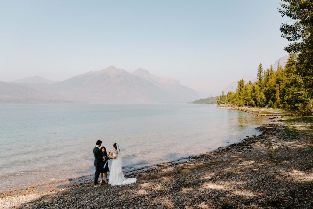 Bride and groom in wedding attire with an officiant during their elopement ceremony at Lake McDonald in Montana.