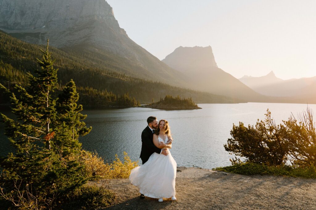 Bride in a white wedding dress twirled into a groom in a black suit at sunset at Sun Point in Glacier National Park 