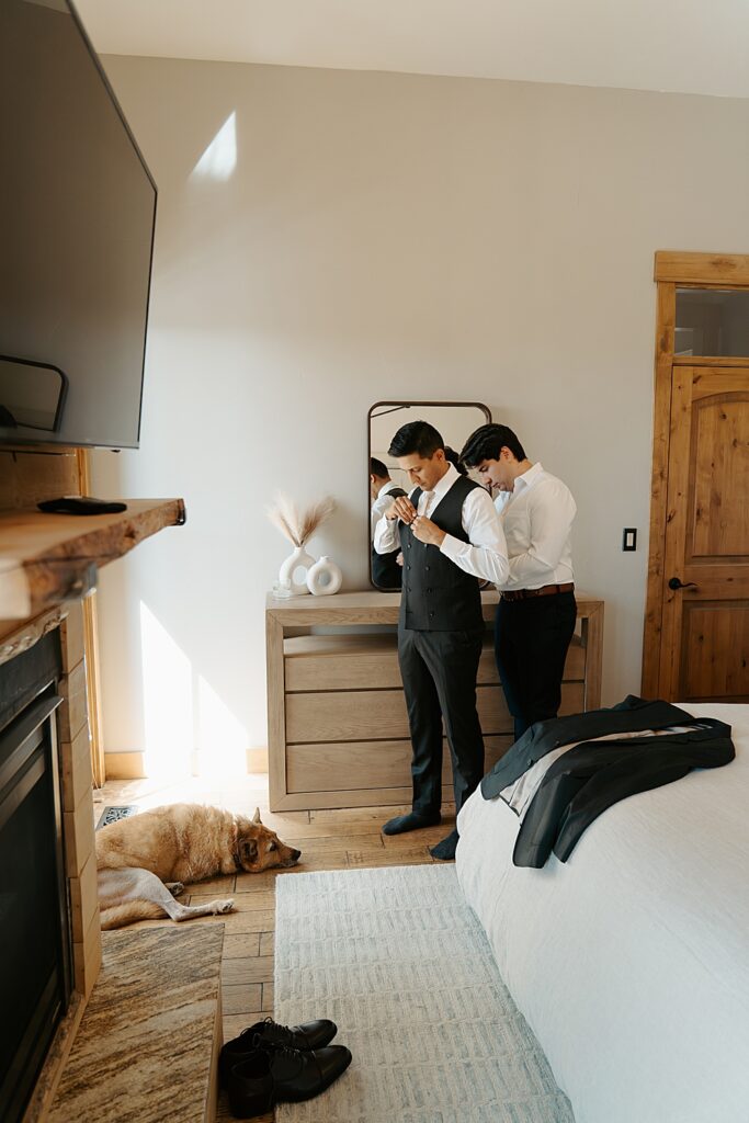 Best man helping the groom get ready in an Airbnb with the groom's dog laying on the floor in front of them. 
