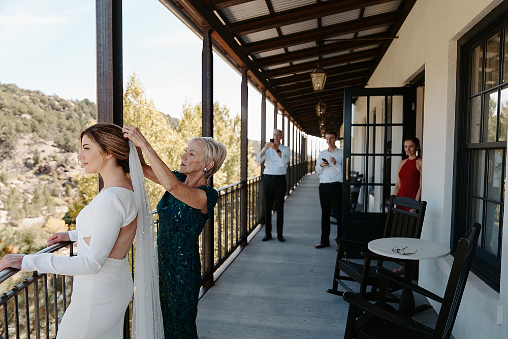 Mother of the bride helping the bride put on her veil at Surf Hotel in Buena Vista, Colorado. The bride's dad, brother, and best friend are watching in the background. 
