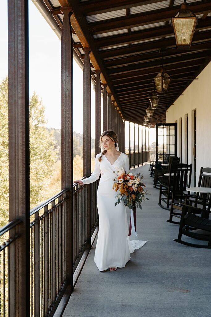 Bride in a white, long sleeve wedding dress walking on an outdoor balcony with a large, fall bridal bouquet. 