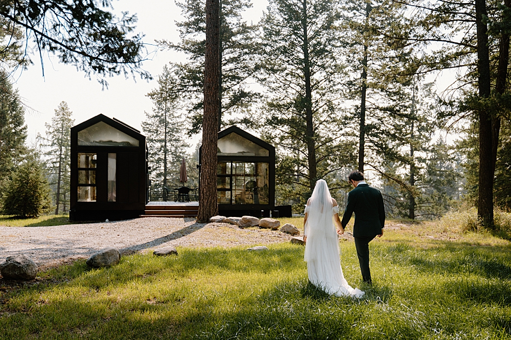 Bride and groom holding hands and walking in the grass towards their cute tiny home rental in Columbia Falls, MT.