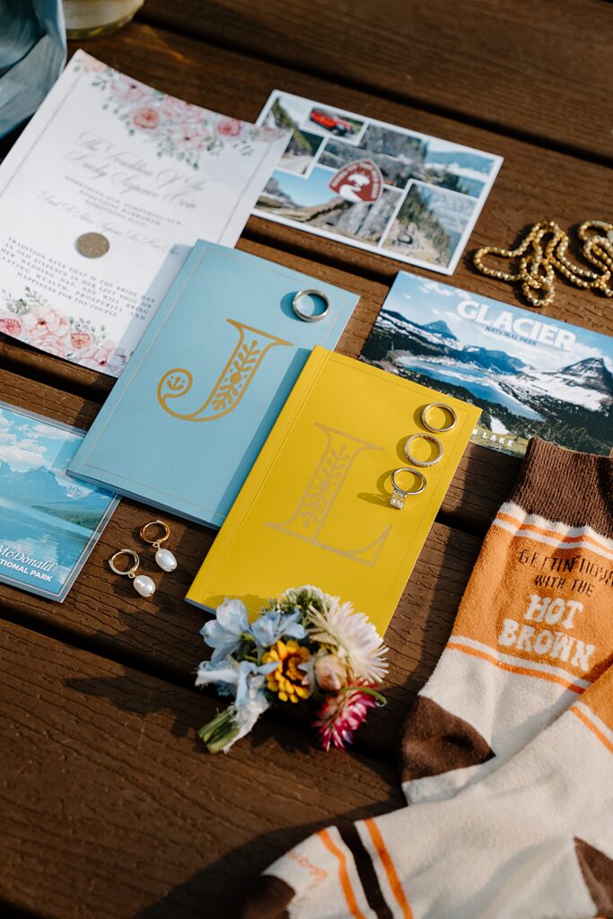 Wedding details with a blue vow book and yellow vow book, yellow gold wedding rings, jewelry, wedding invitation, and tall socks. 