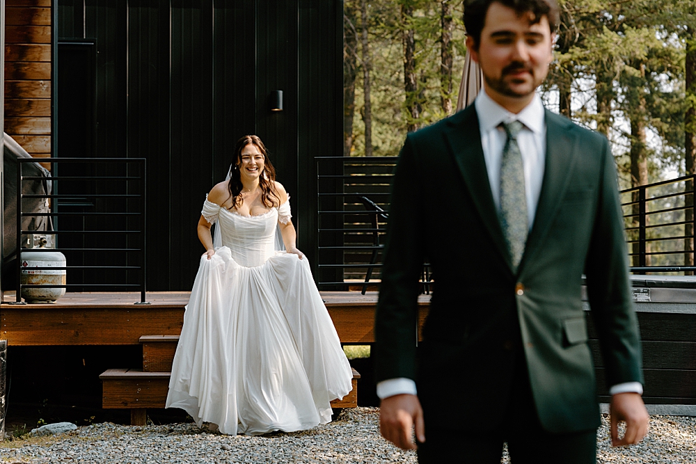 Bride in a corset off-the-shoulder a-line wedding dress holding her skirt and walking towards the groom who is facing the camera for a surprise "first look."