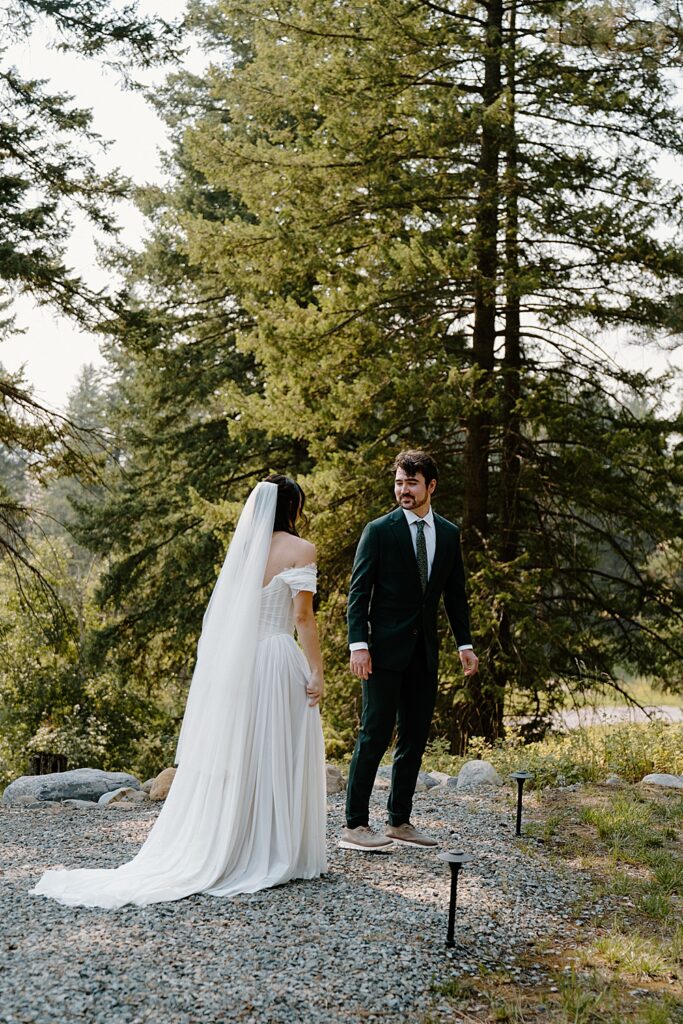 Groom in a green wedding suit turning around to see his bride in an a-line dress with a veil for the first time.