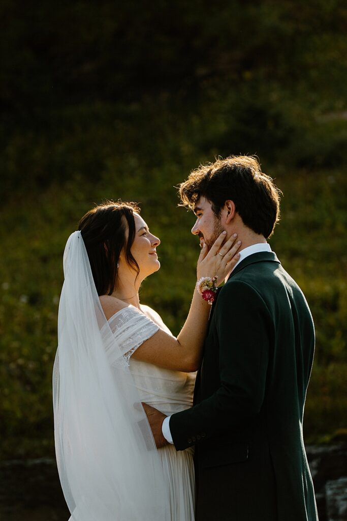 Bride in an off-the-shoulder dress and veil holding her groom's face at their elopement. 