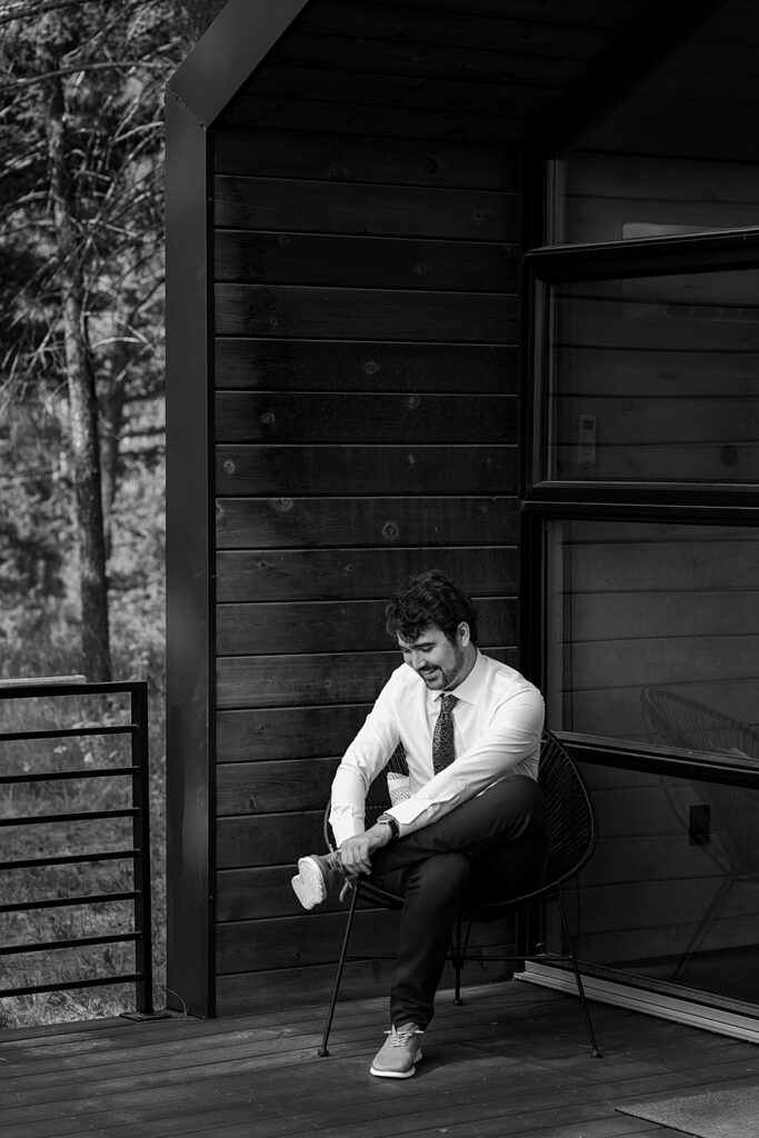 Black & white of groom getting shoes on in front of tiny home in Columbia Falls, MT. 