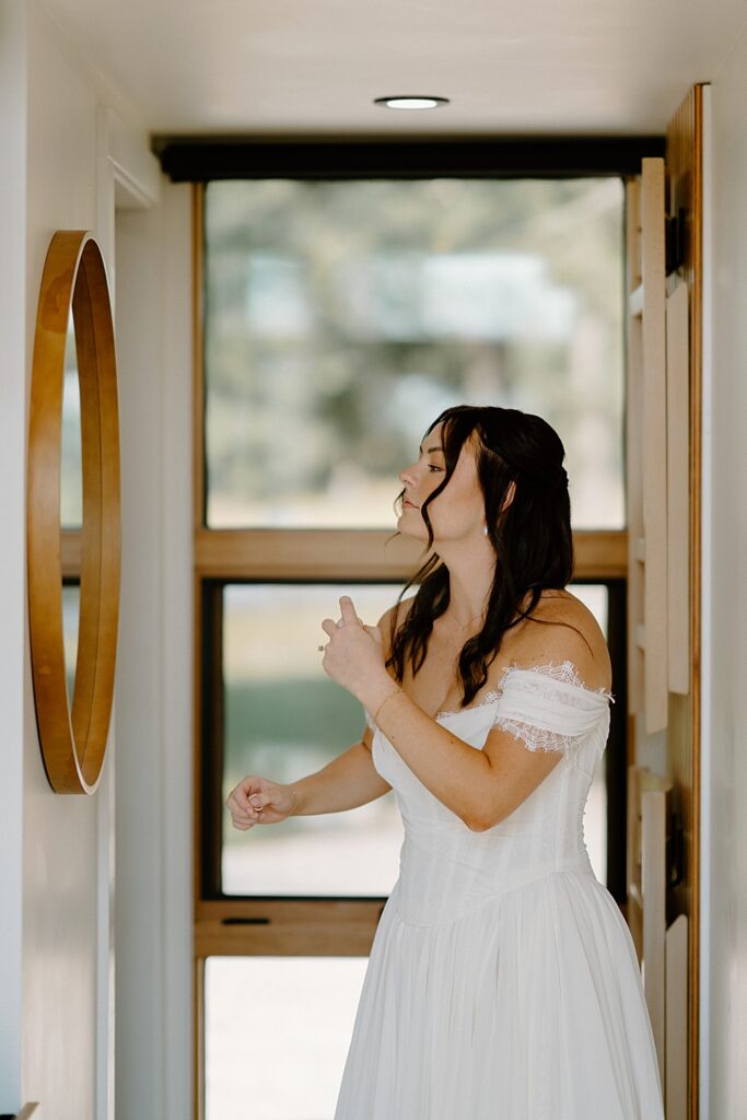 Bride in a white wedding dress looking in a mirror and applying perfume.