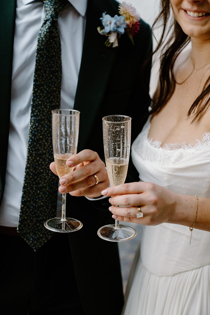 Up-close of bride and groom holding plastic sparkly champagne flutes after toasting their elopement. 