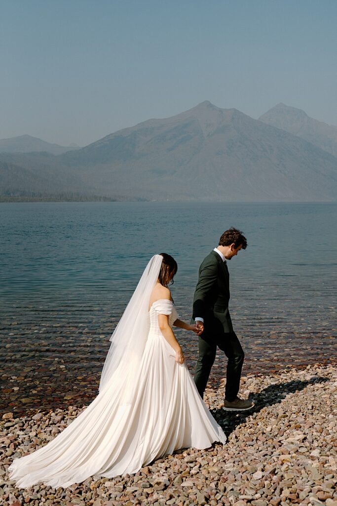 Elopement couple holding hands and walking on the shore at 10-Mile Pullout, Lake McDonald in Glacier National Park. 