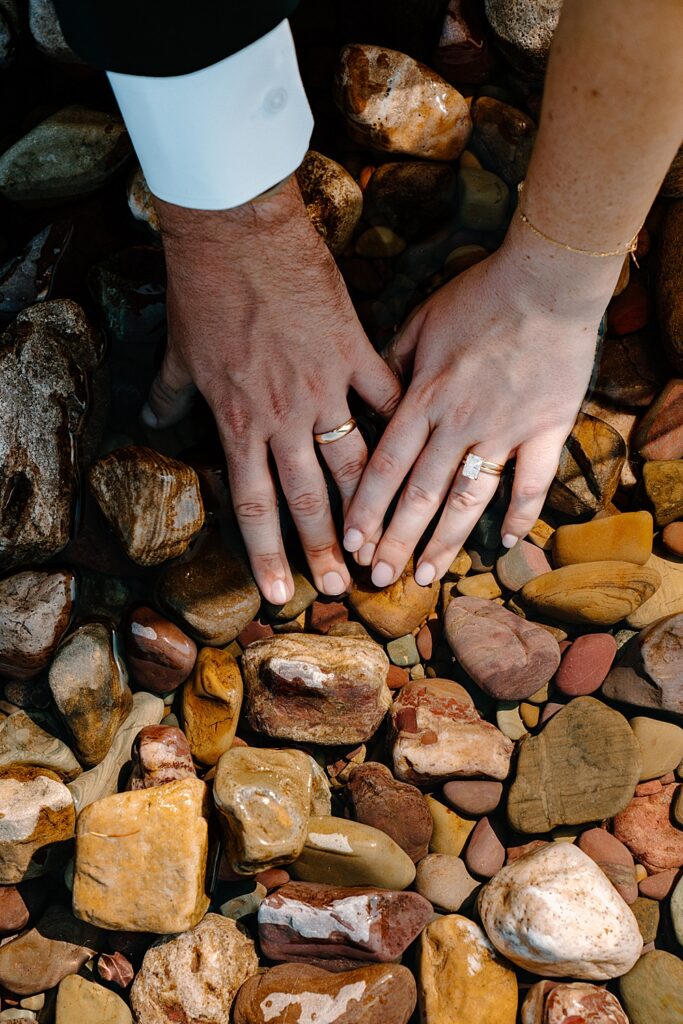 Bride and groom with yellow gold wedding rings putting their hands in the water at Lake McDonald. 