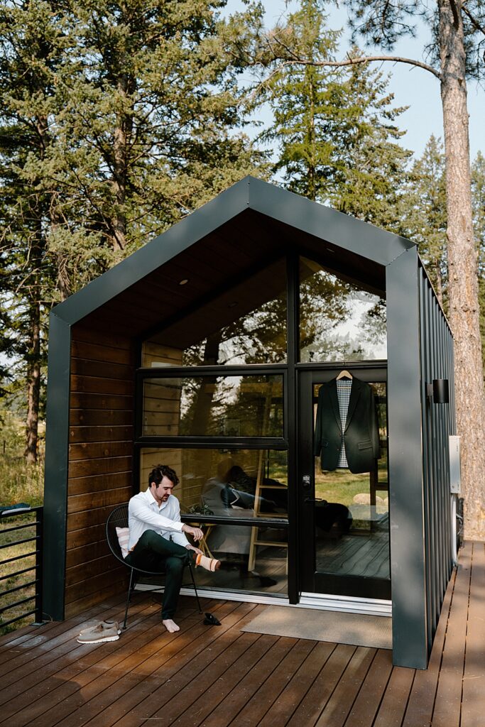 Groom putting his shoes on outside a tiny cabin in Flathead Valley before his Montana adventure elopement.