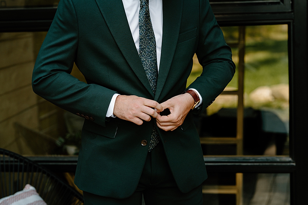 Groom buttoning his green wedding suit jacket