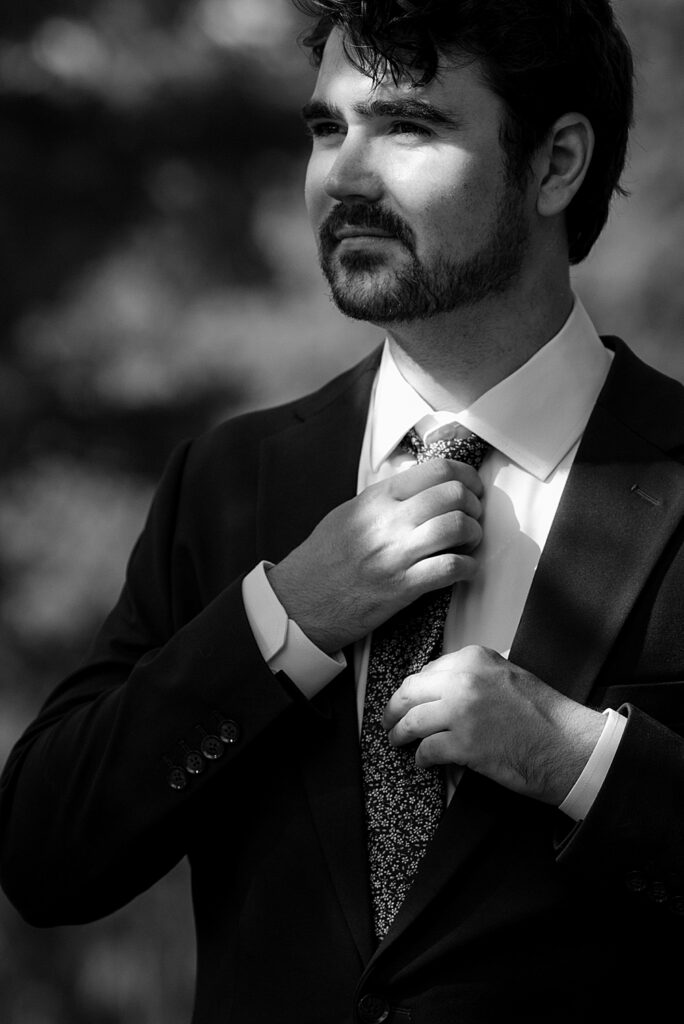 Black & white of groom adjusting his floral wedding tie