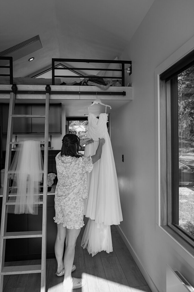 Black & white of bride adjusting her hanging wedding dress