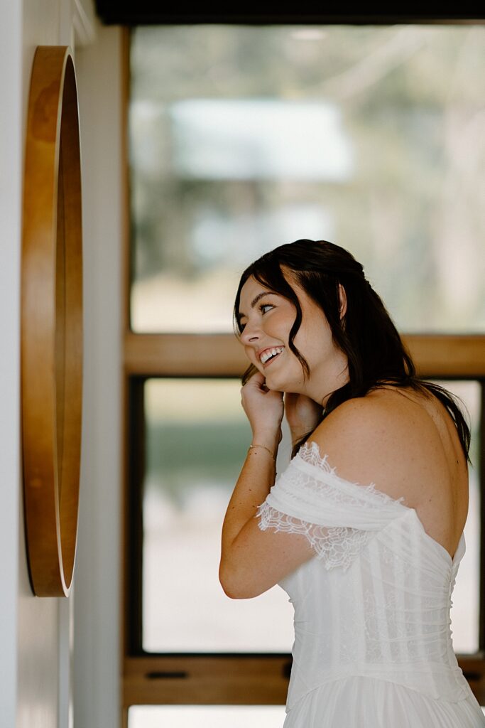 Bride putting her earrings on in front of a mirror