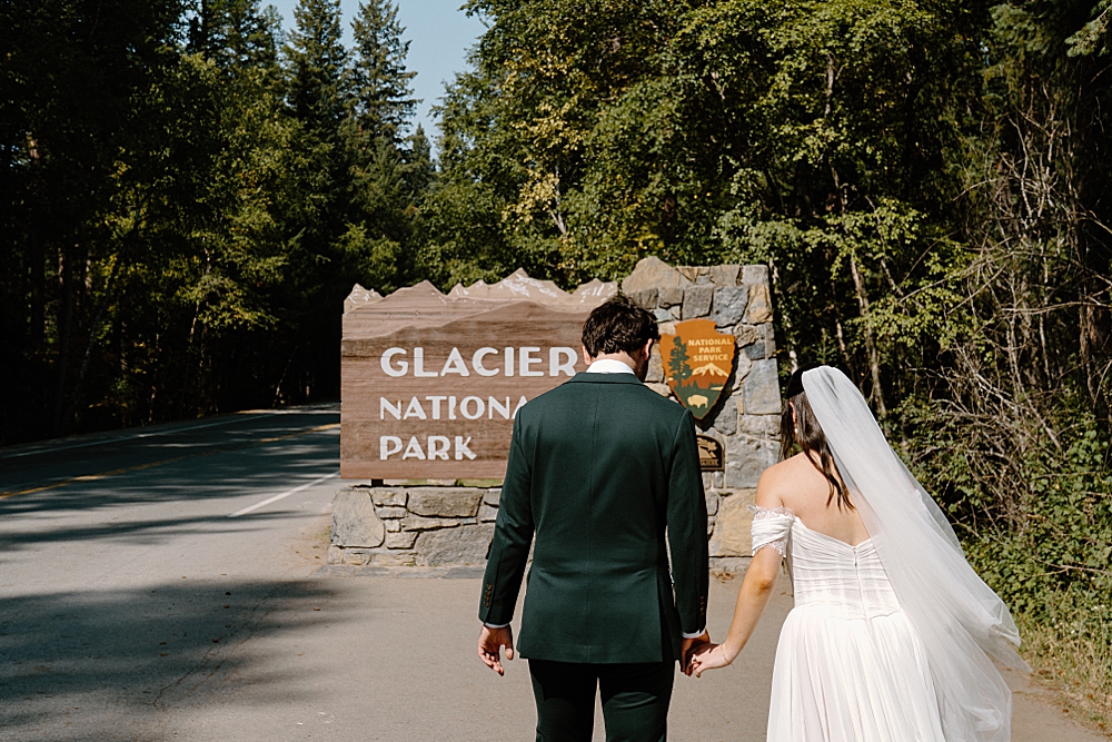 Glacier National Park sign with elopement couple holding hands