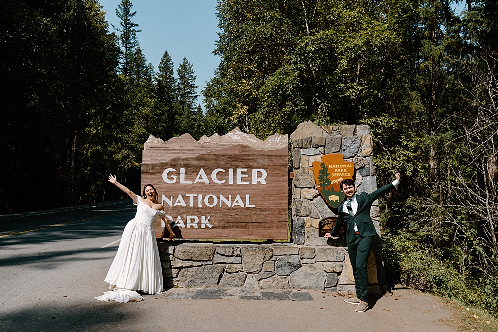 Bride and groom cheering in front of National Park sign at Glacier Park, Montana