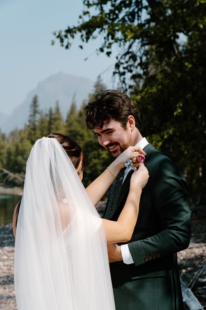 Bride helping put a colorful boutonniere on groom at Lake McDonald
