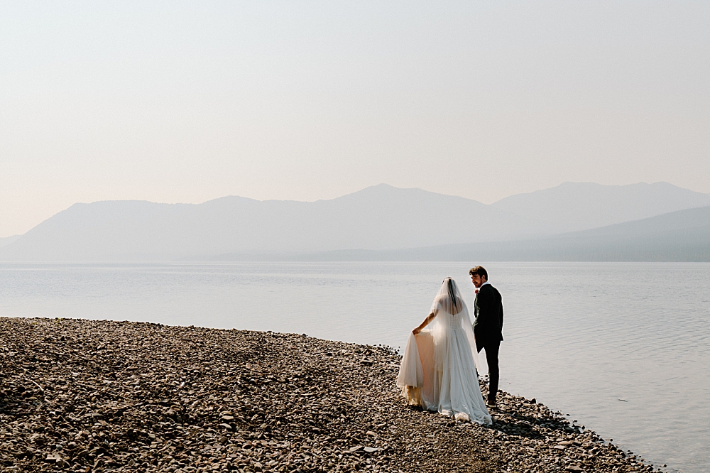 Bride and groom walking along the rocky shore at 10-mile pullout, Lake McDonald