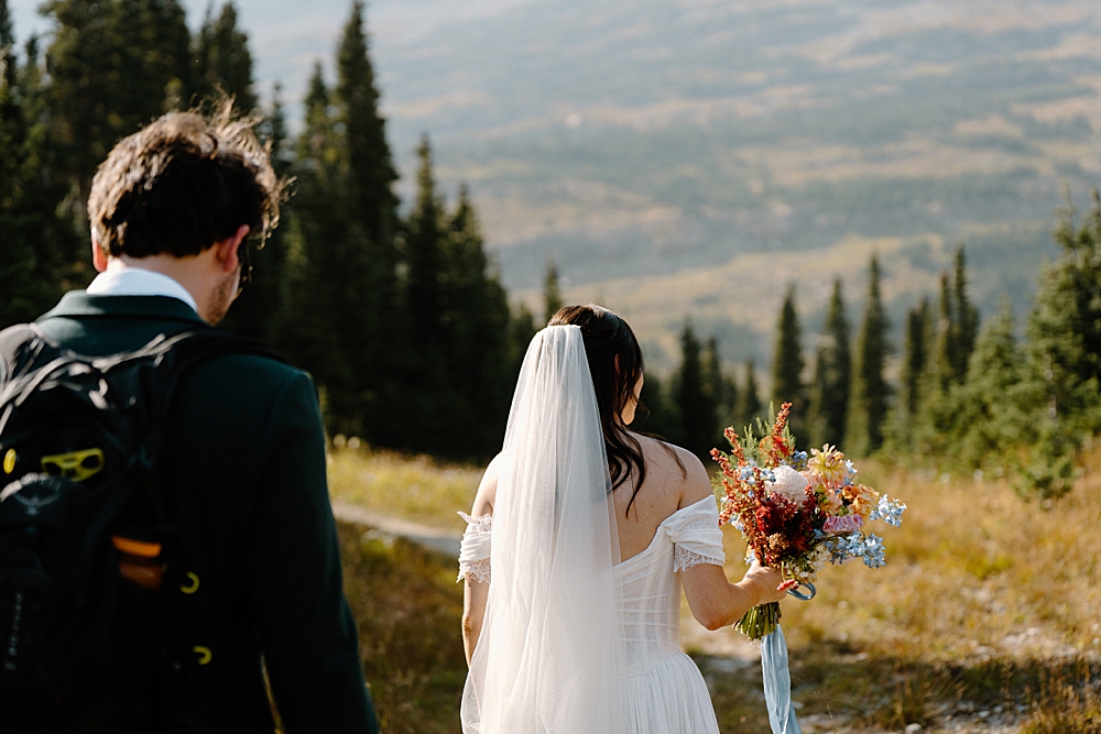 Bride holding a colorful bridal bouquet and groom with a hiking pack