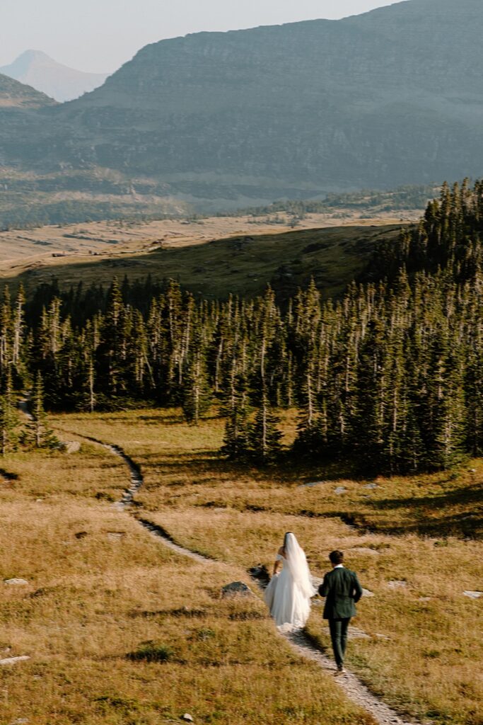 Bride and groom running along a trail in Glacier Park for their elopement adventure