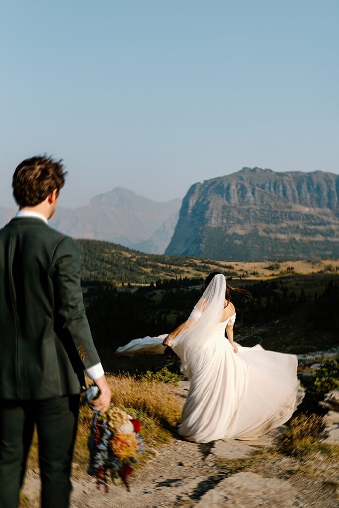 Groom holding bridal bouquet facing bride while she twirls her dress train