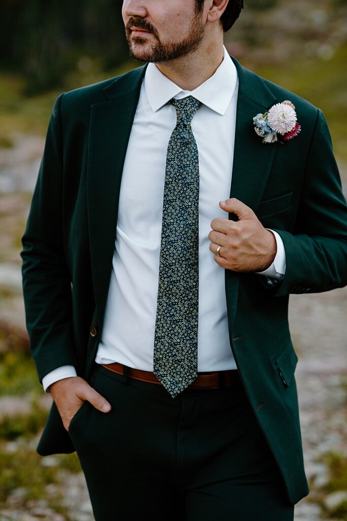Groom in a green suit holding his lapel with a yellow gold wedding band on