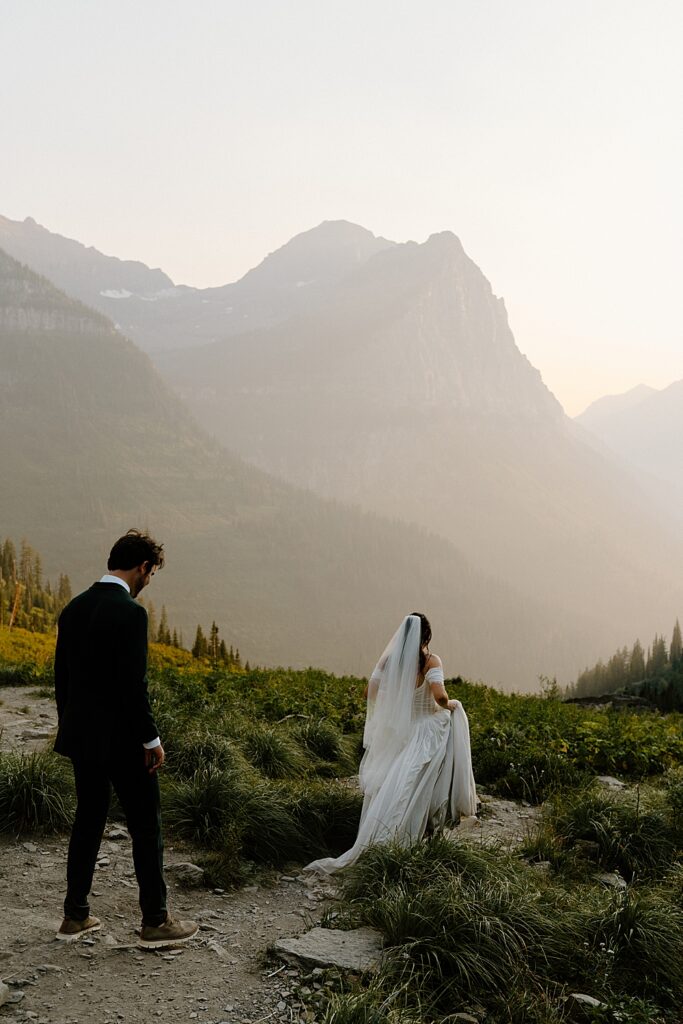 Bride walking down a dirt path with groom following behind at Big Bend in Glacier Park