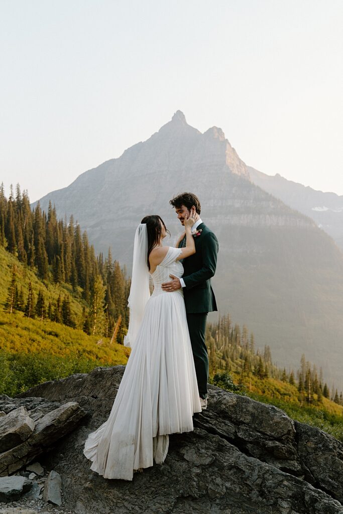 Bride and groom facing each other on a rock at sunset in Glacier Park