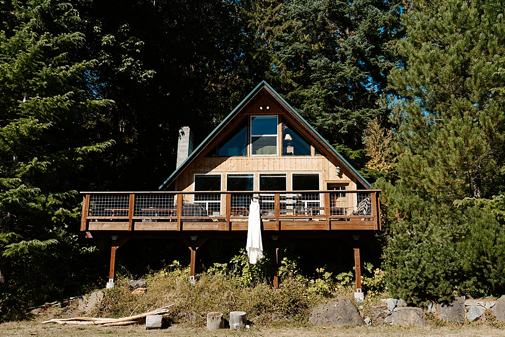 A-frame cabin with a large deck and a satin wedding dress hanging from the railing.