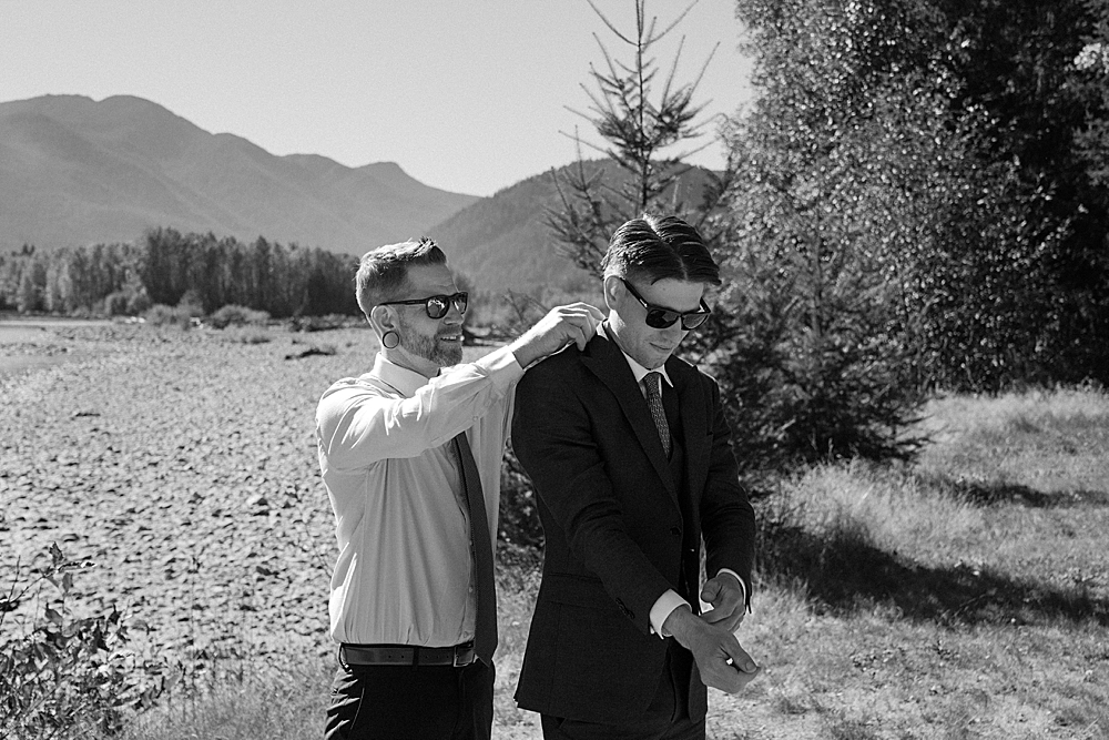 Black & white of father of the groom helping groom with his suit. 
