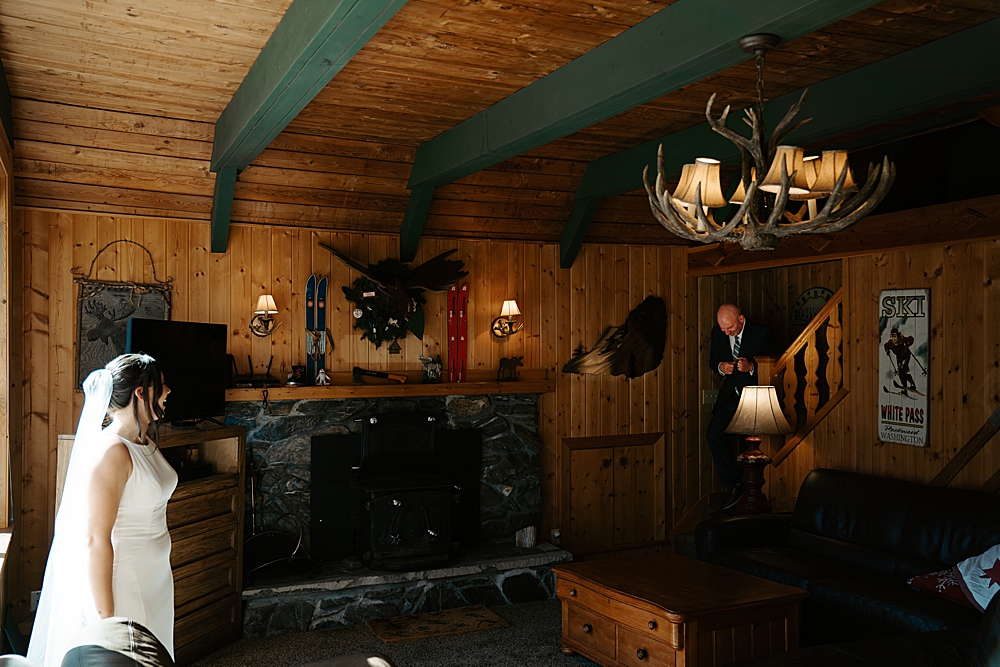Father of the bride walking down the stairs at a cabin to the bride for a first look.