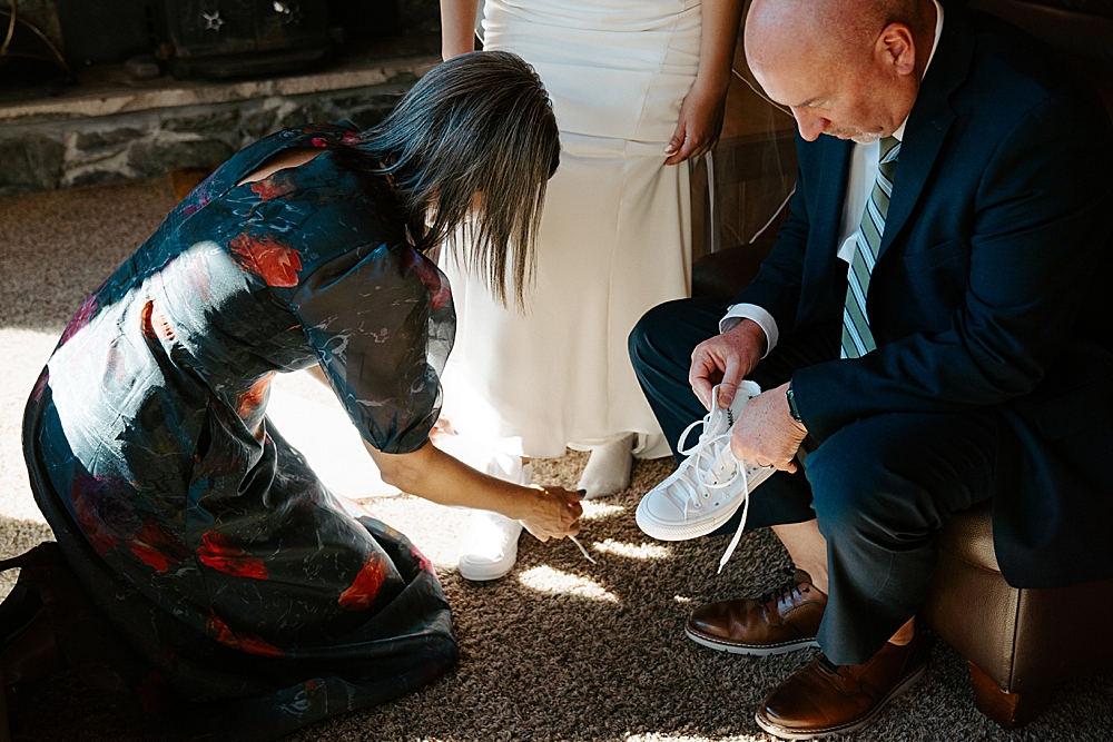 Father and mother of the bride helping the bride into her custom, hand-embroidered white converse.