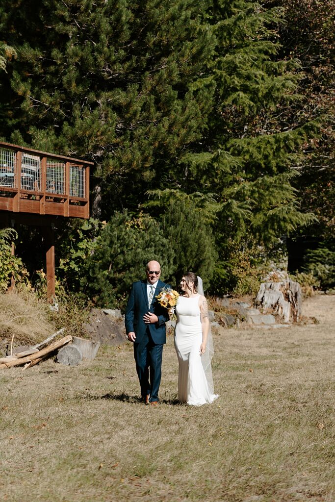 Father of the bride and bride walking on a lawn to the ceremony location.