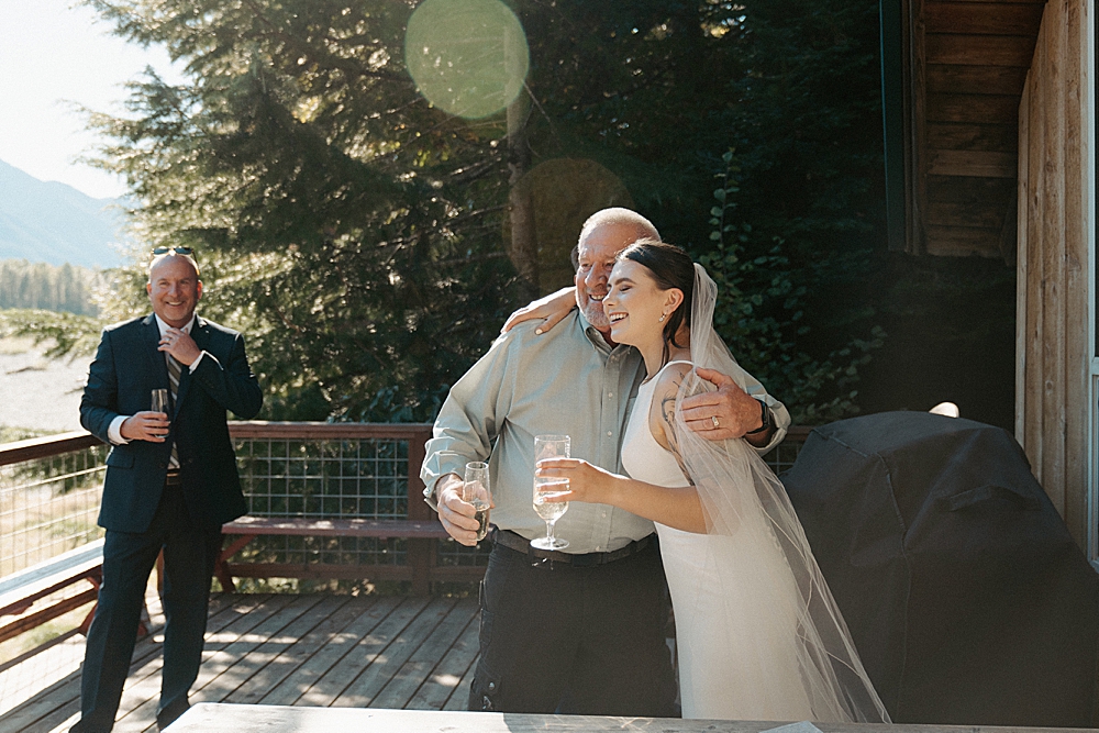 Bride hugging family member on a cabin's deck with champagne glasses in hand.
