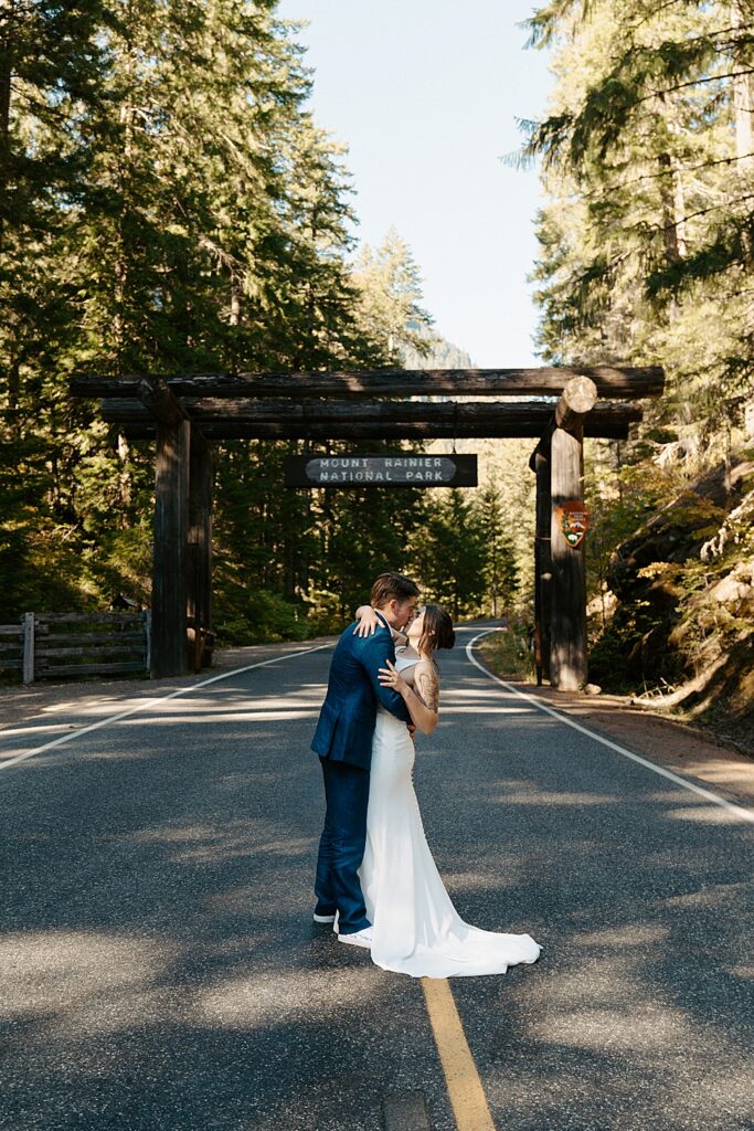 Bride and groom kissing in the road with the Mount Rainier National Park wooden sign behind them.