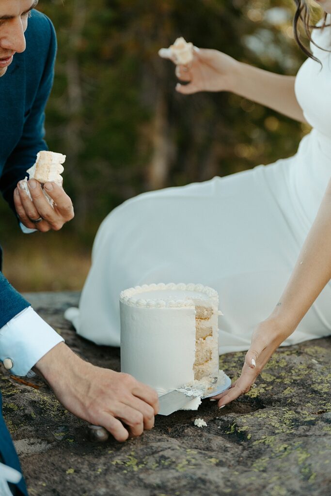 Up close of a white wedding cake with a bride and groom holding slices of cake in their hands.